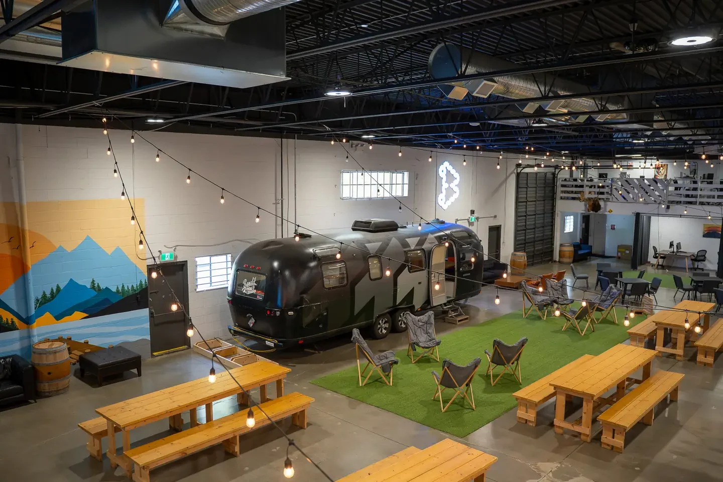 Site B hall with picnic tables, string lights and an Airstream